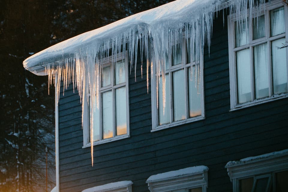 Long icicles hanging from the snow-covered eave of a dark clapboard house